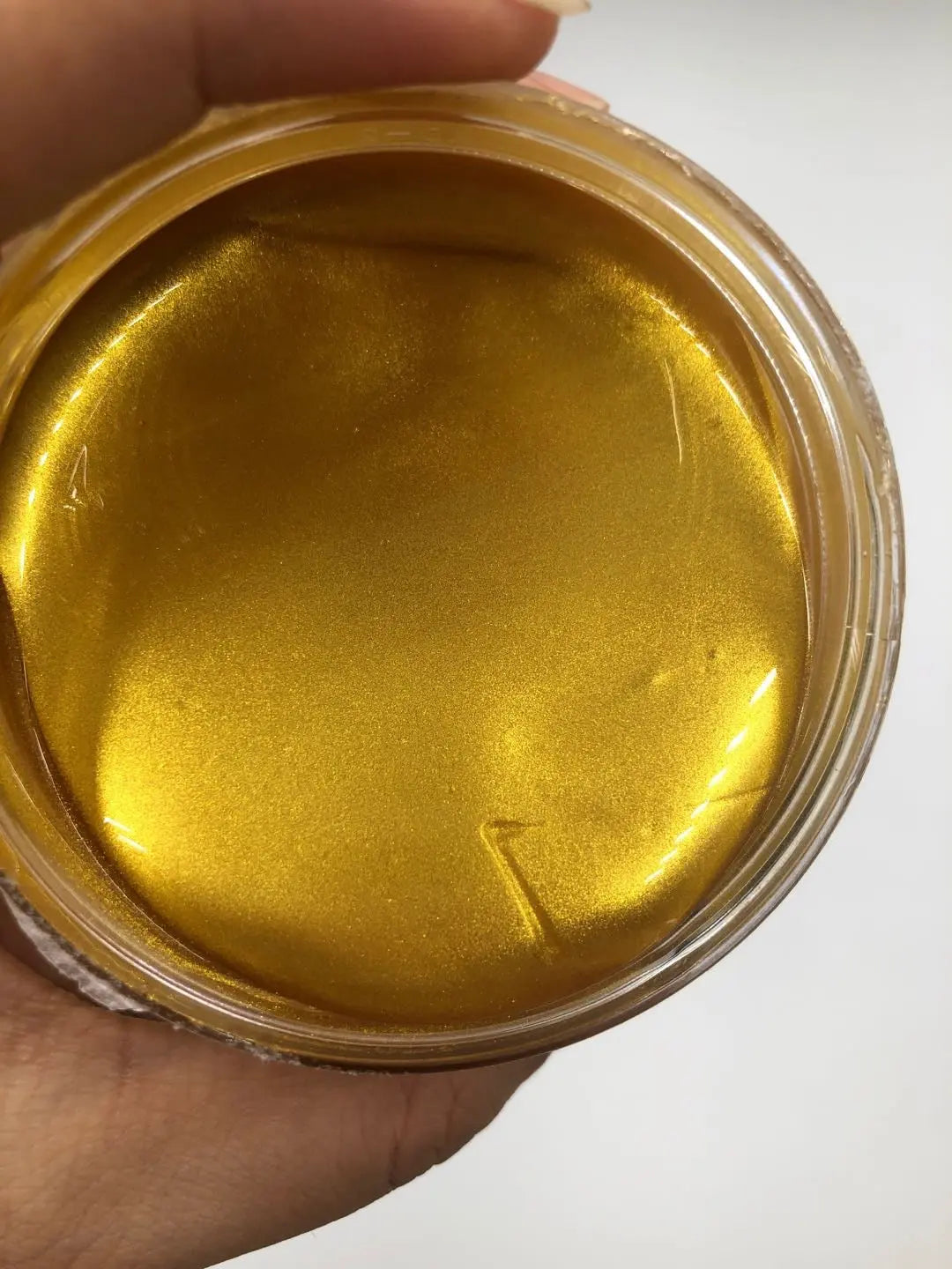 Gold-colored substance in a jar held by a hand on a white background